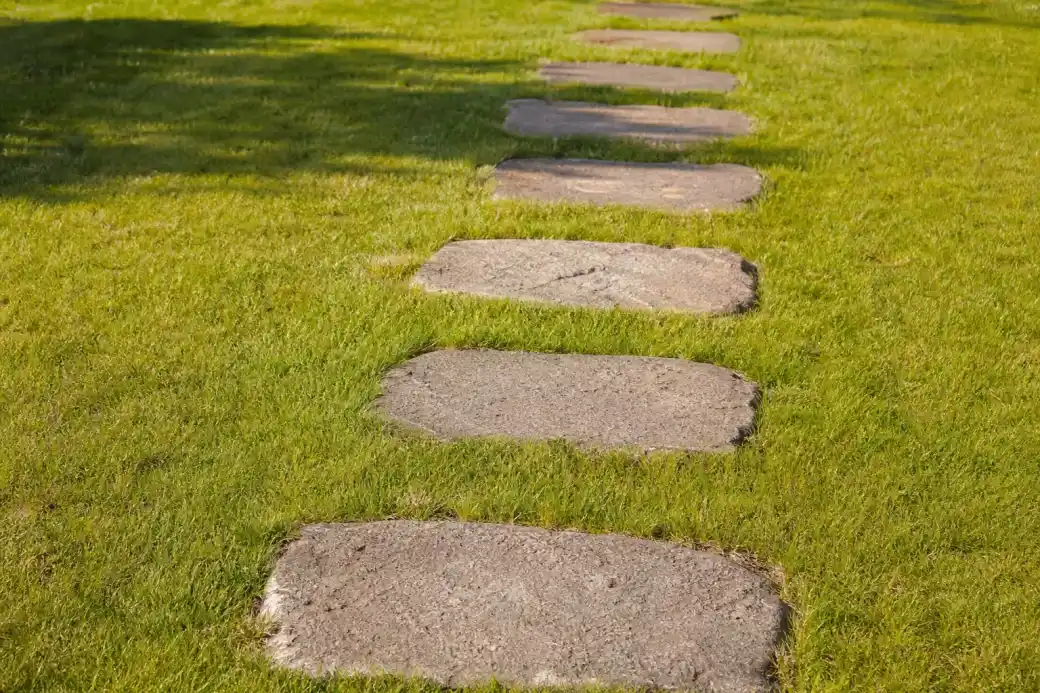Pas japonais en pierre posés de niveau dans une pelouse verte sur sol sableux, espacement régulier, herbe nette autour de chaque dalle.