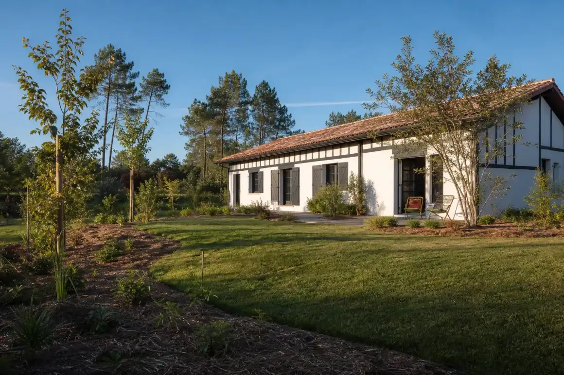 Photo grand angle d'un jardin paysager fraîchement créé devant une maison landaise, pelouse dense, massifs paillés et jeunes arbres, lumière douce de fin d'après-midi, ciel dégagé du Sud-Ouest.